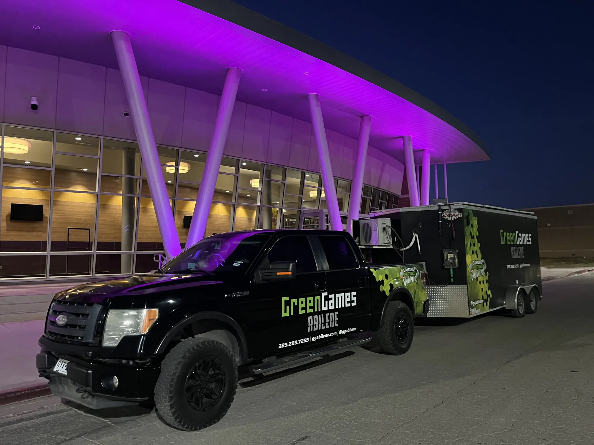 Green Games truck and trailer outside a venue lit in purple